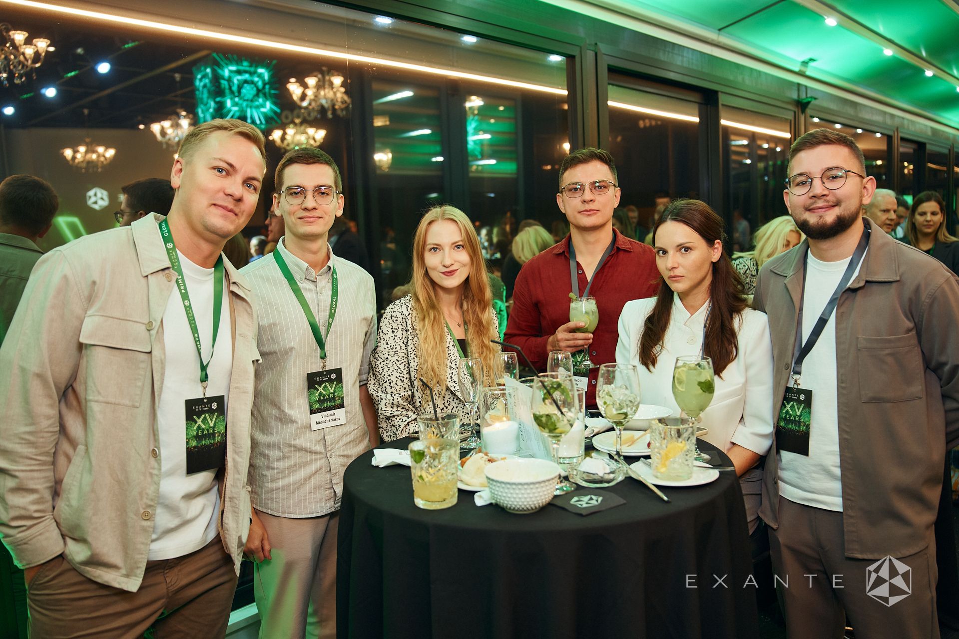 Six people stand behind a black table with drinks at an event with an "XV Years" Exante logo.