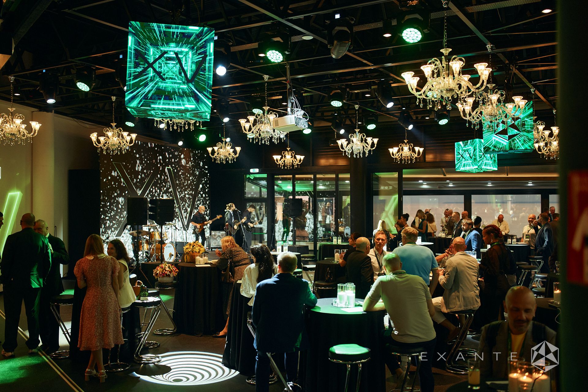 Attendees socialize and listen to a live band during a "XV" branded event in a decorated, dimly lit venue.