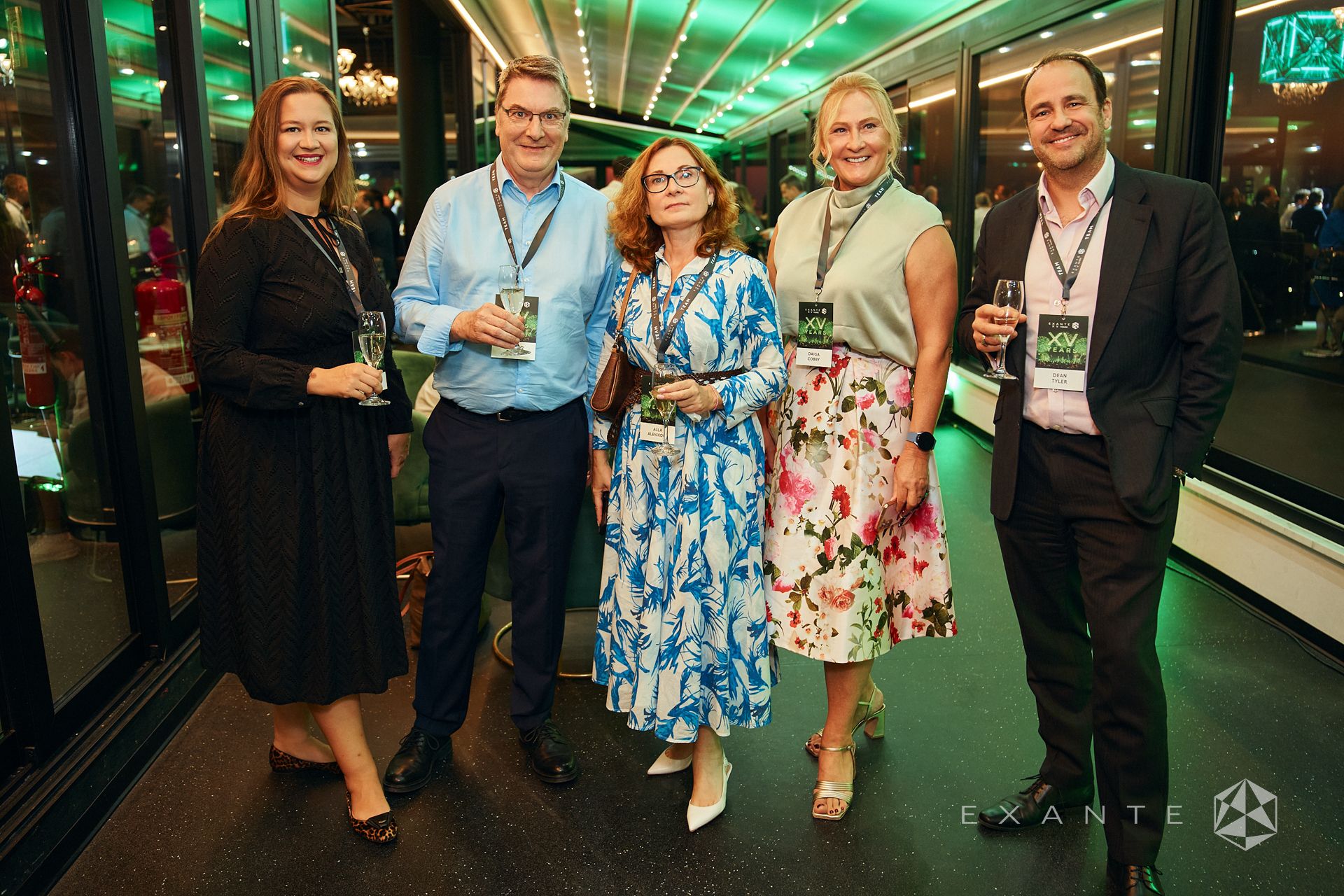 Five professionals, wearing "XV YEARS" conference badges, stand together and pose for a group photo at an evening event.