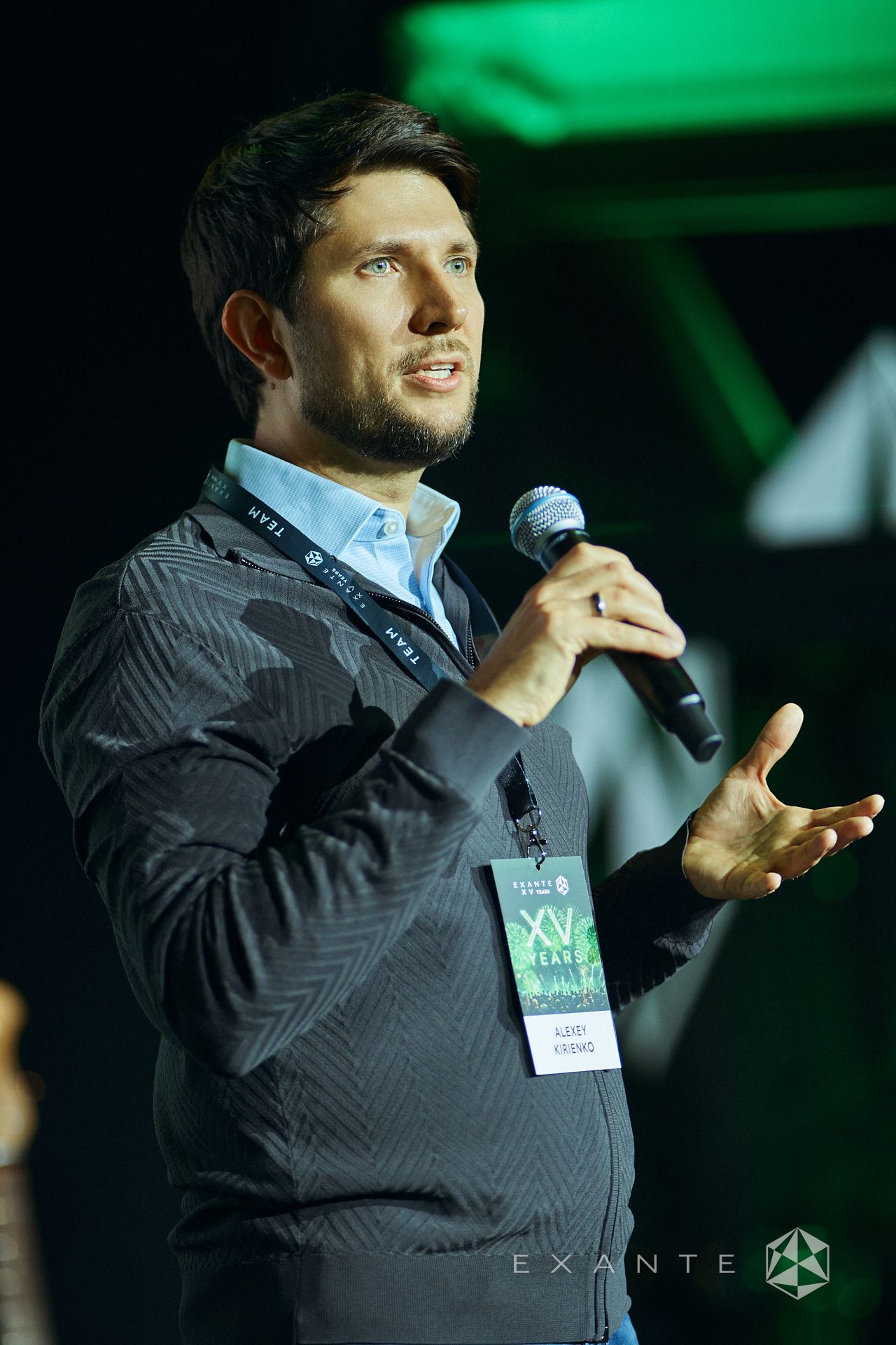 Alexey Kirienko speaks into a microphone at an EXANTE XV Years event, wearing a lanyard with his name tag.