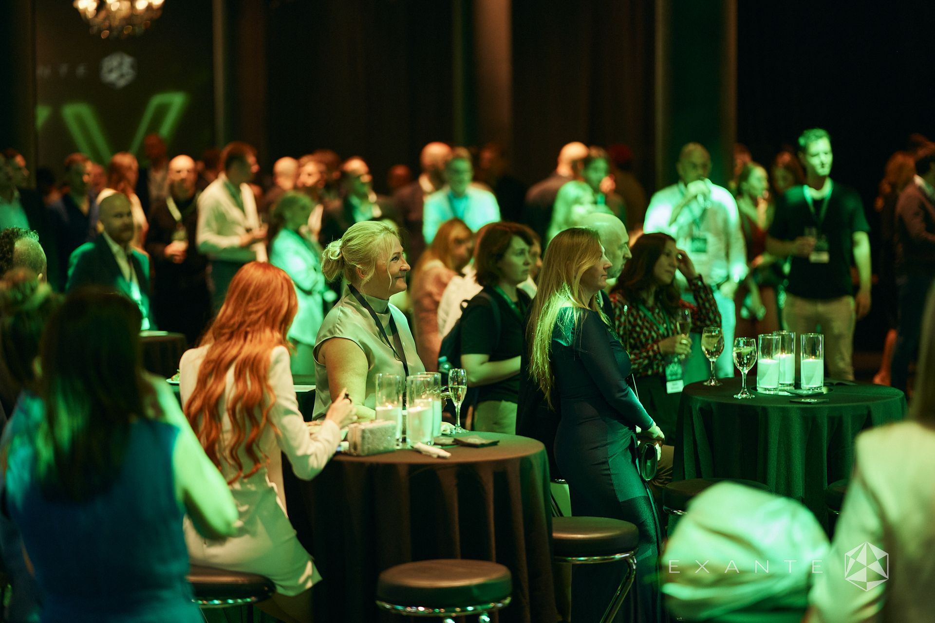 Attendees mingle and socialize at a dimly lit EXANTE networking event with circular tables and green ambient lighting.