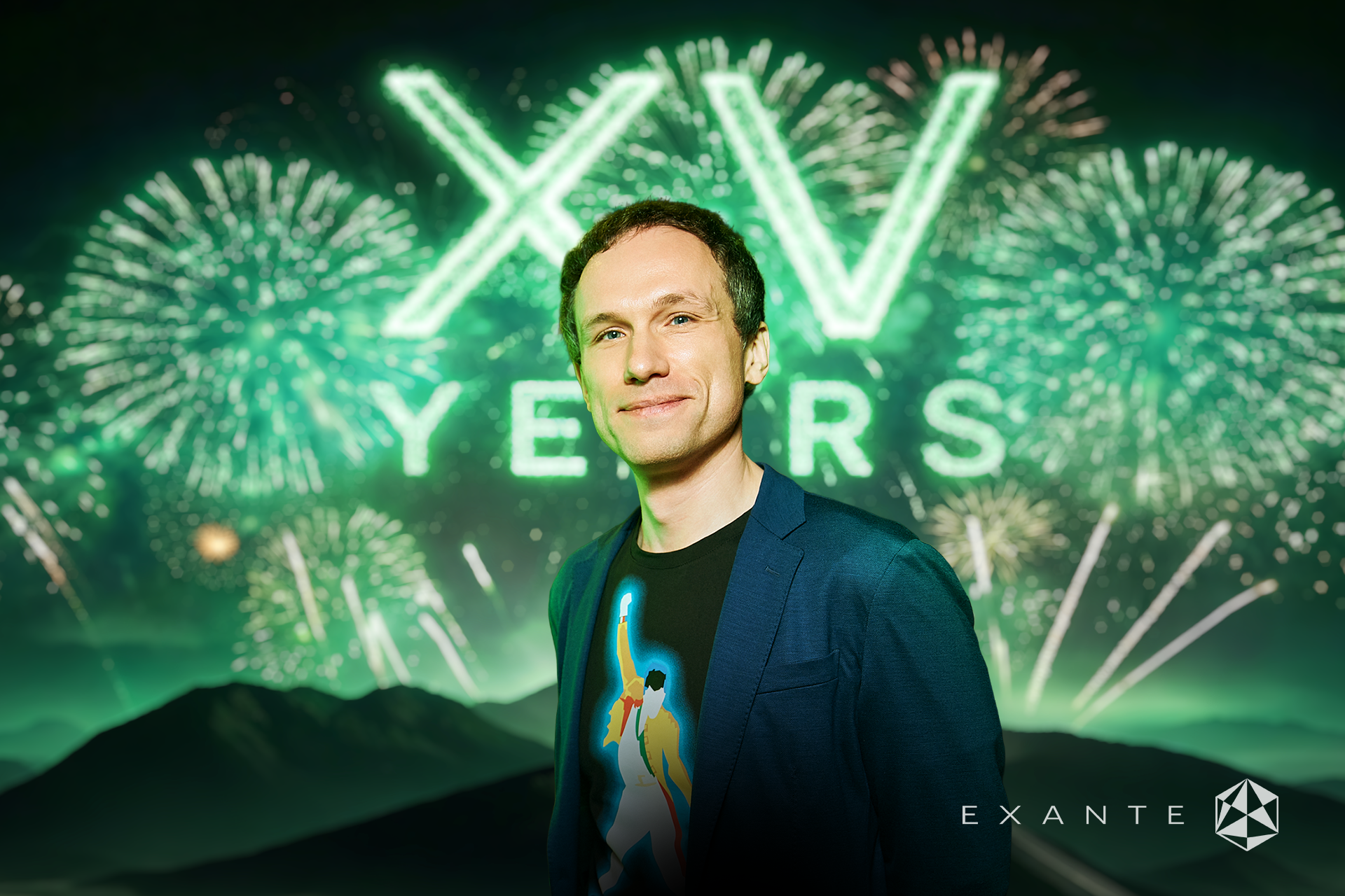 A man in a blue blazer and Queen t-shirt stands before a screen displaying "XV YEARS" and fireworks.